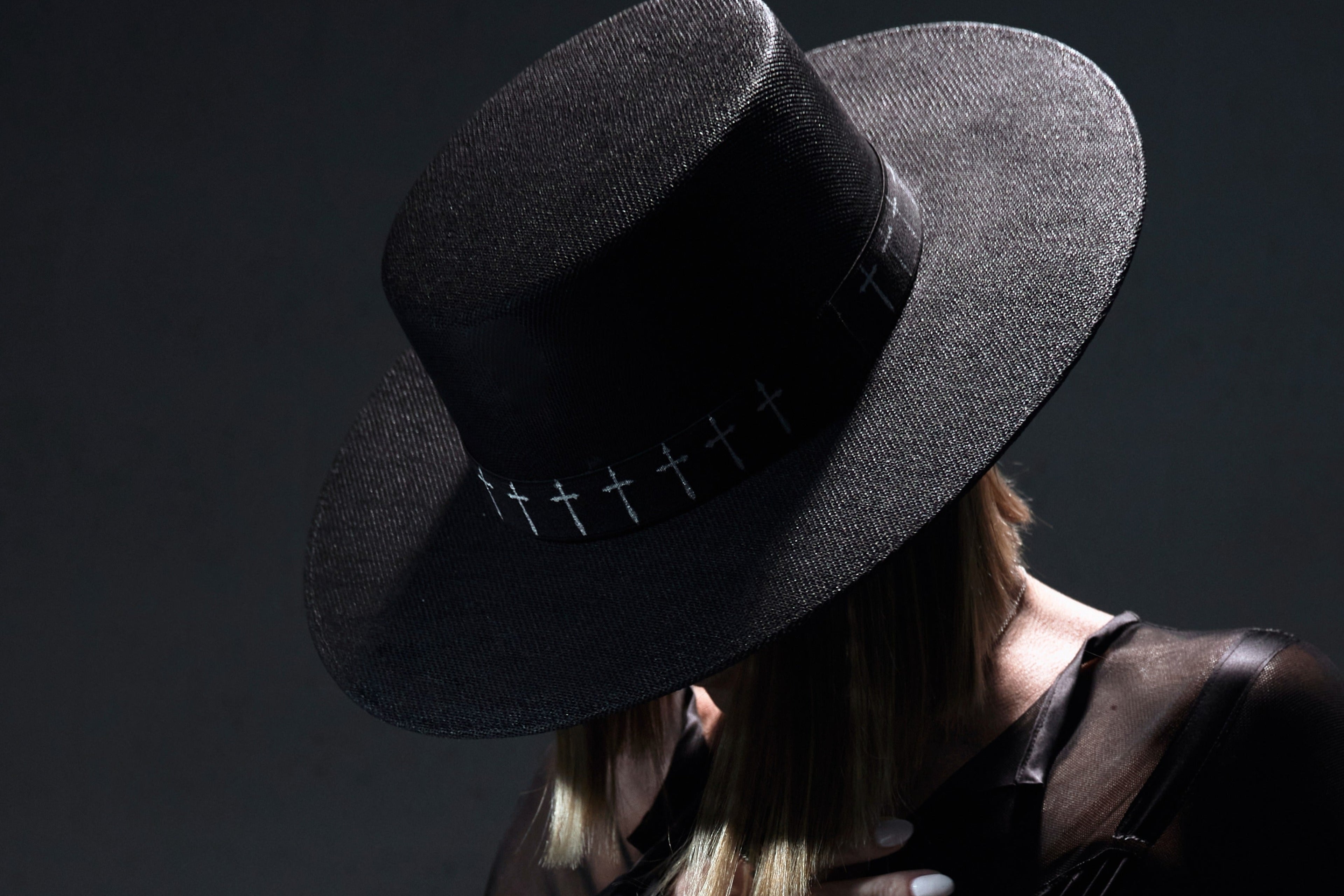 Person wearing a black hat with cross details against a dark background
