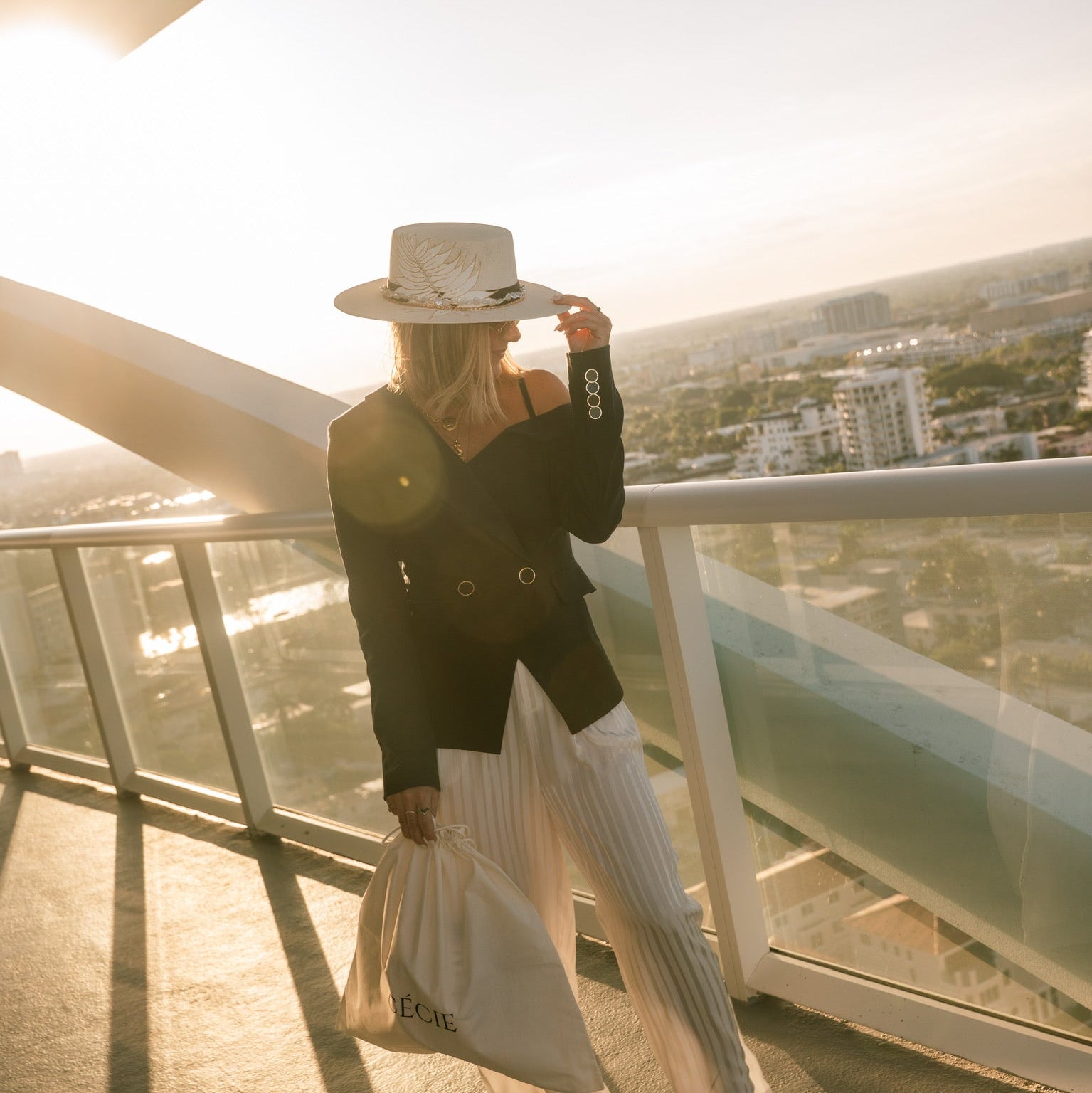 Person standing on a balcony with a cityscape view during sunset.