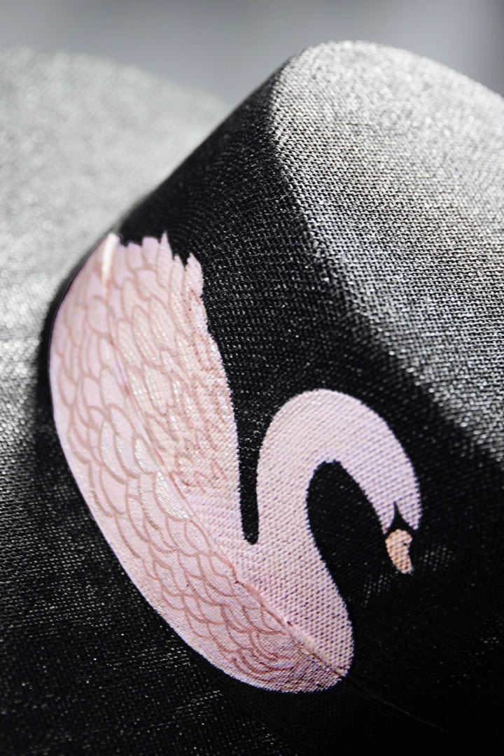 Black hat with pink swan embroidery on a gray background