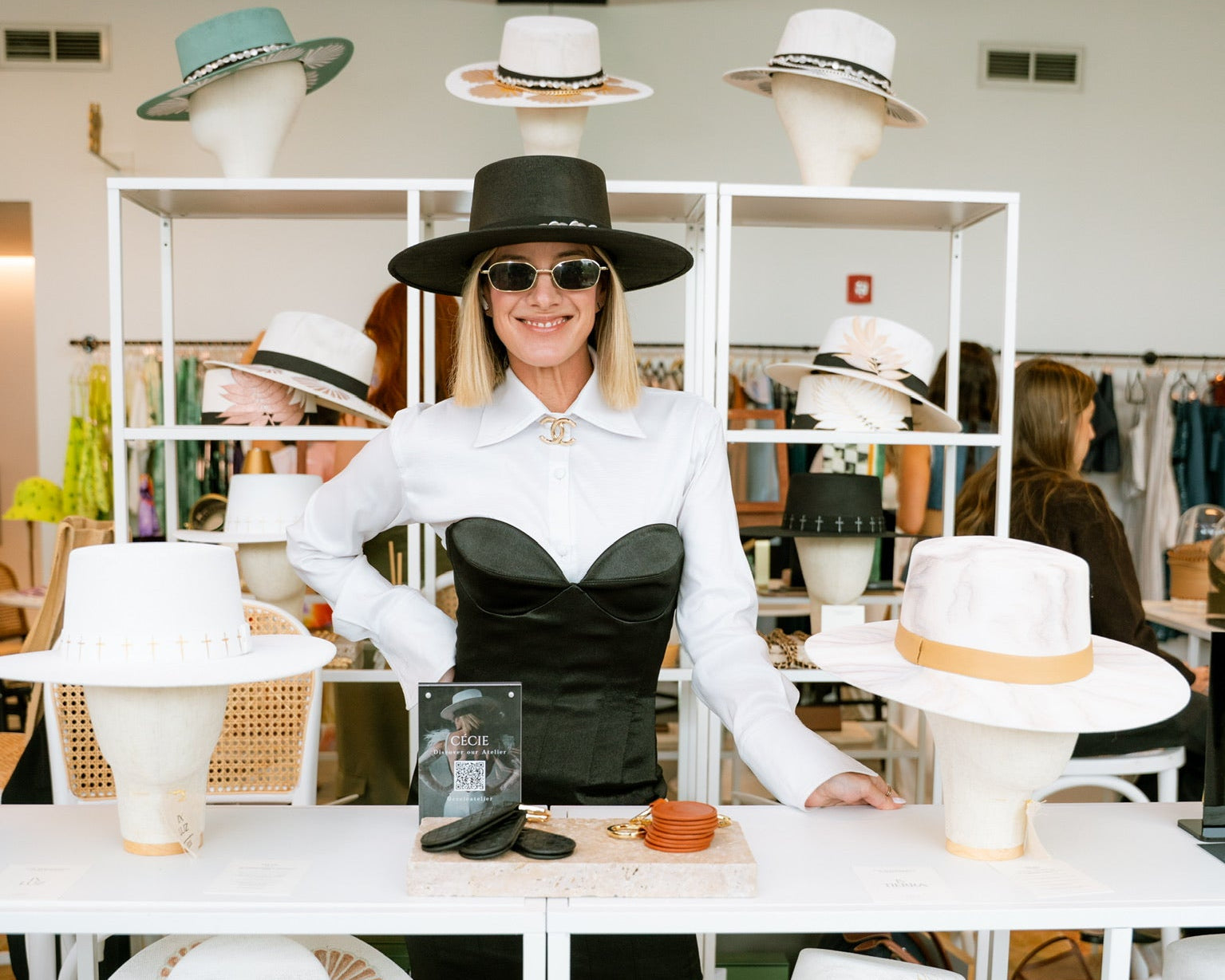 Woman in a stylish outfit with hats displayed around her in a store setting