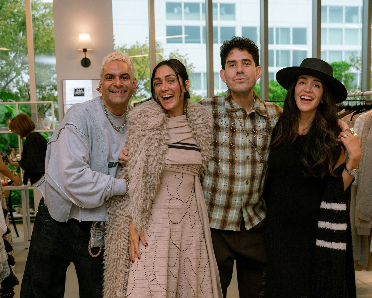Four people posing together in a modern indoor setting with large windows.