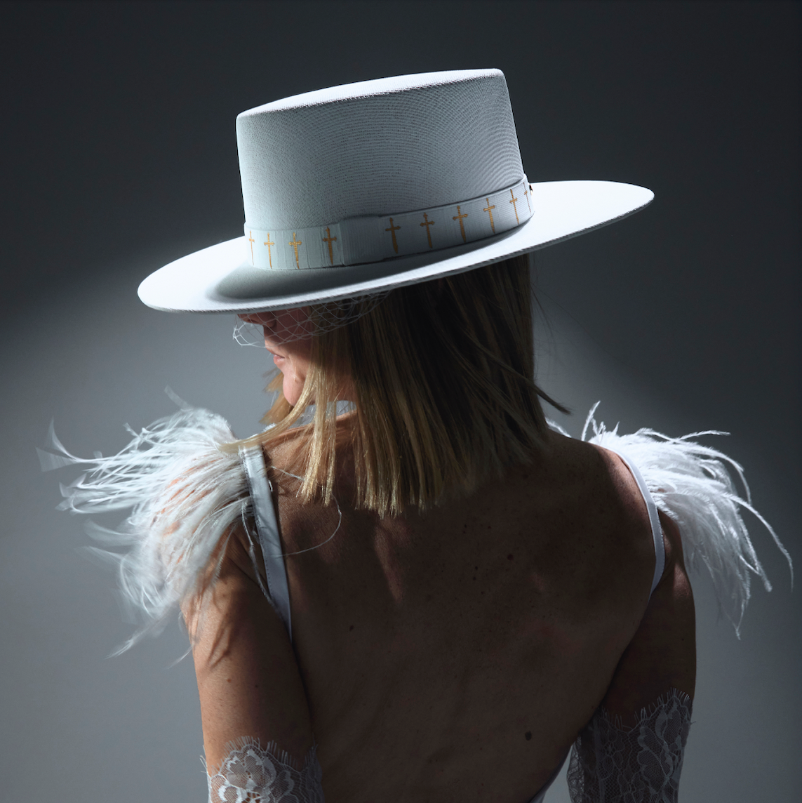 Person wearing a white hat with feathered shoulders against a dark background