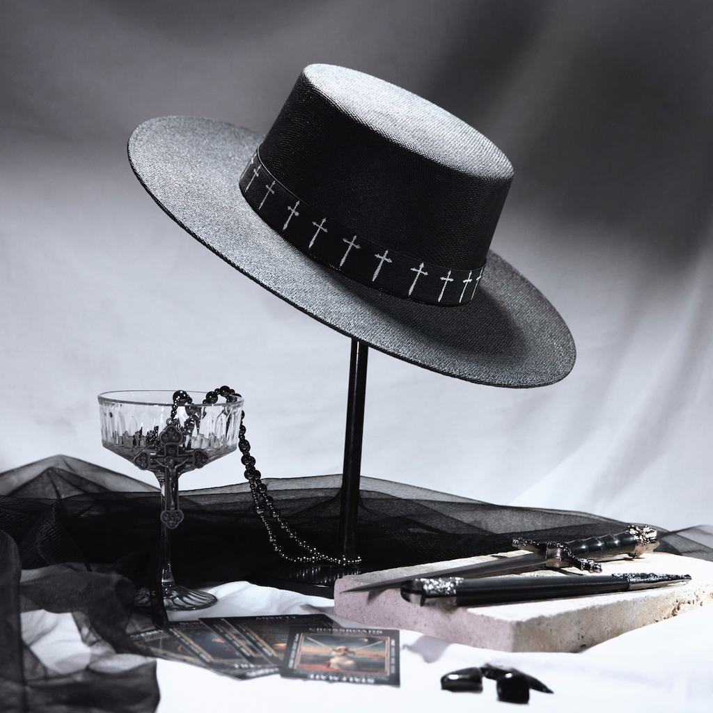 Black hat with decorative band on a stand, surrounded by vintage items on a reflective surface.
