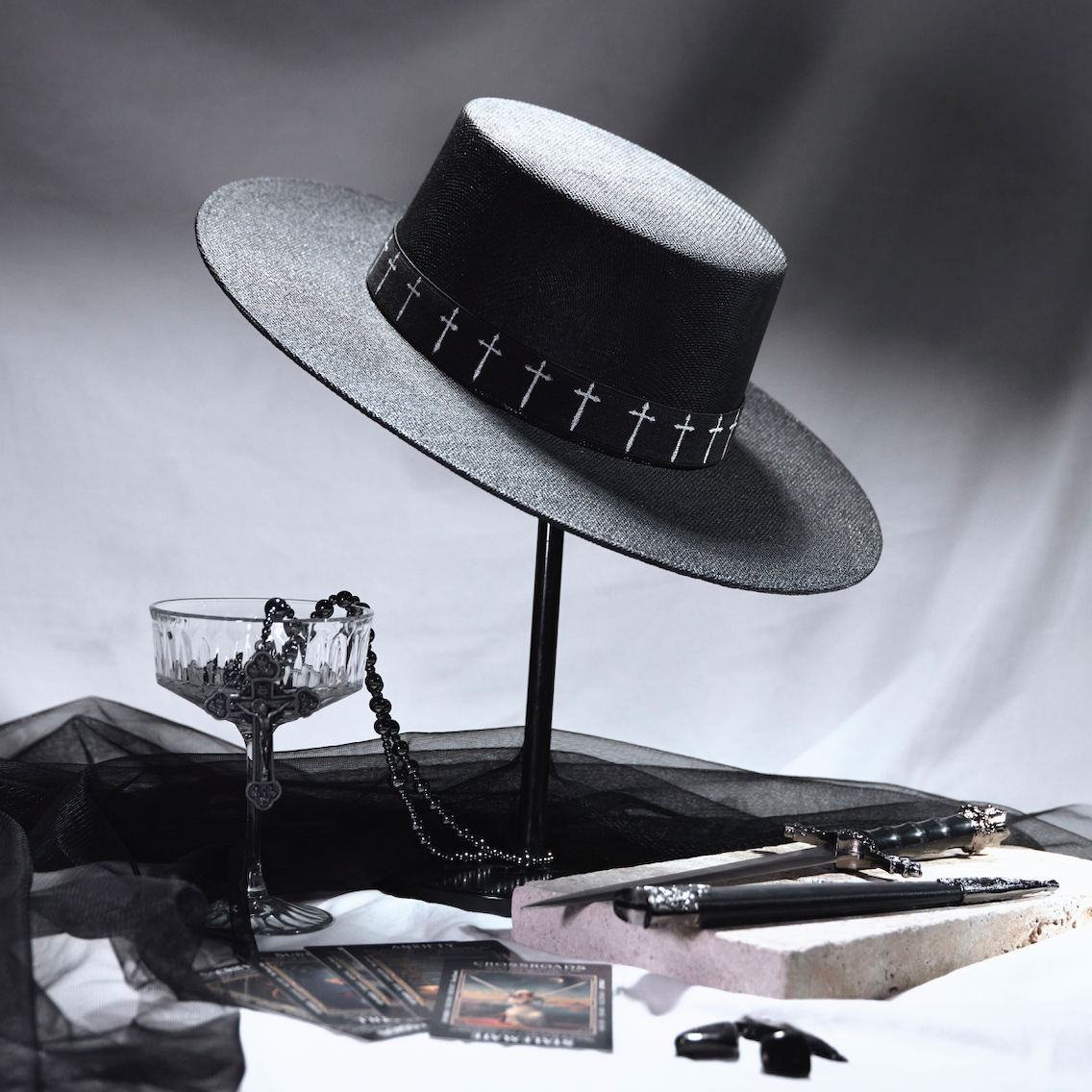 Black hat with decorative band on a stand, surrounded by vintage items on a reflective surface.