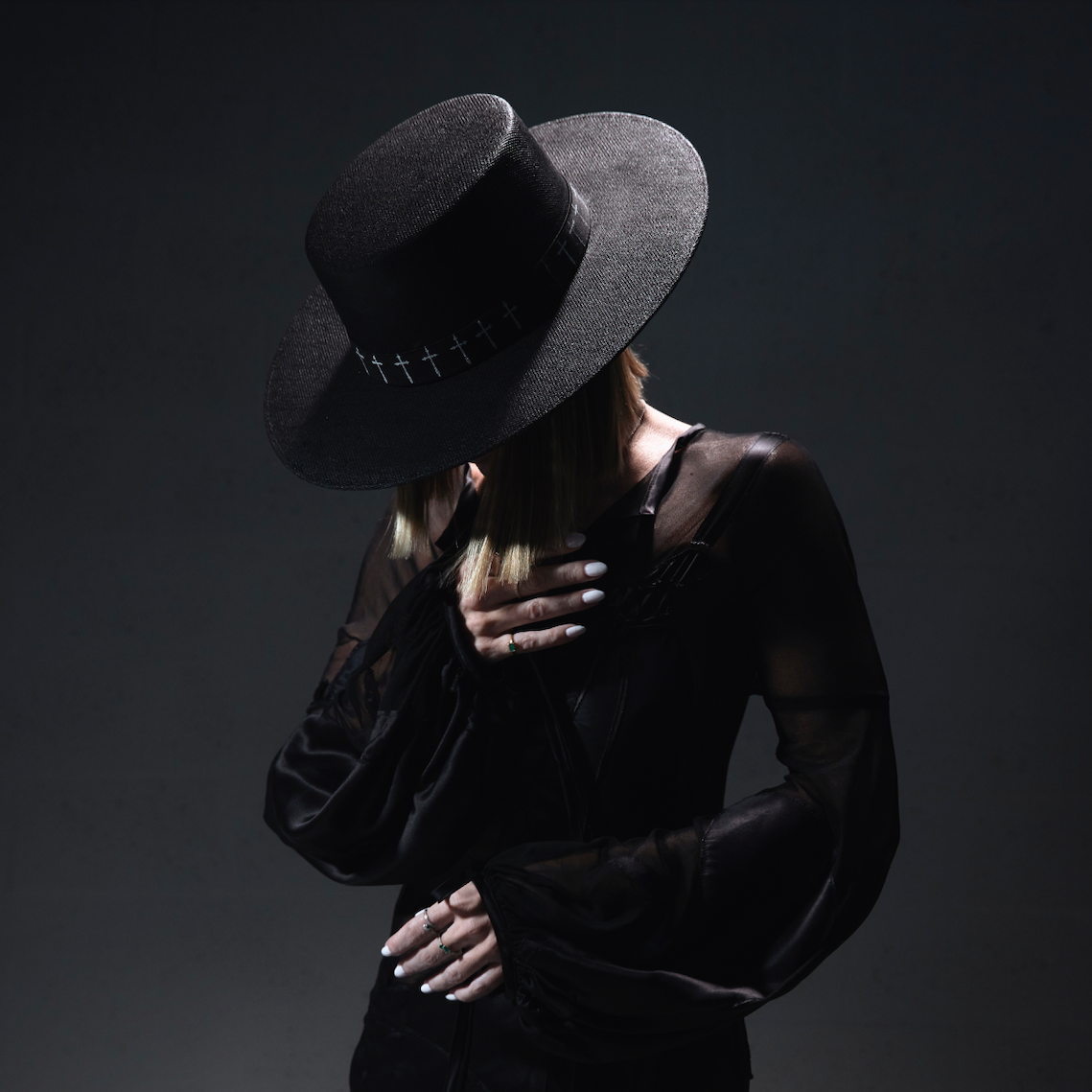 Person wearing a dark hat and black outfit against a dark background