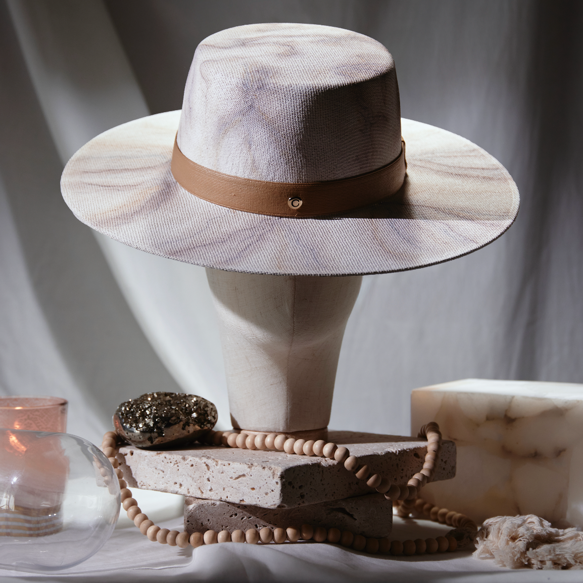 White hat with brown band on a stand with decorative items on a dark background